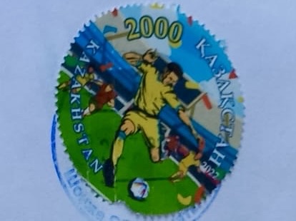 A colorful postage stamp from Kazakhstan featuring a soccer player in action, with the year '2000' and festive decorations in the background.